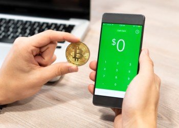 Picture of hand holding a bitcoin with Square's Cash App's buy bitcoin page on a mobile phone