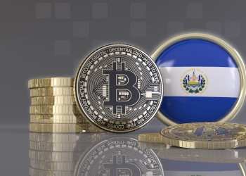 Picture of a round El Salvador flap with a silver bitcoin next to it, and a stack of coins behind the bitcoin