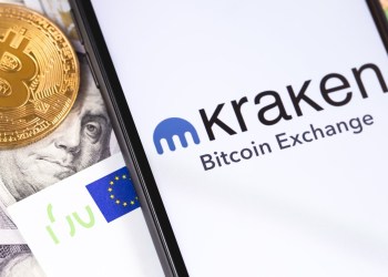 Picture of a gold bitcoin next to a smart phone with the Kraken app open on it