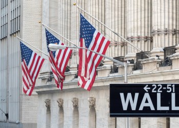 Picture of a Wall Street street sign with three American flags behind it